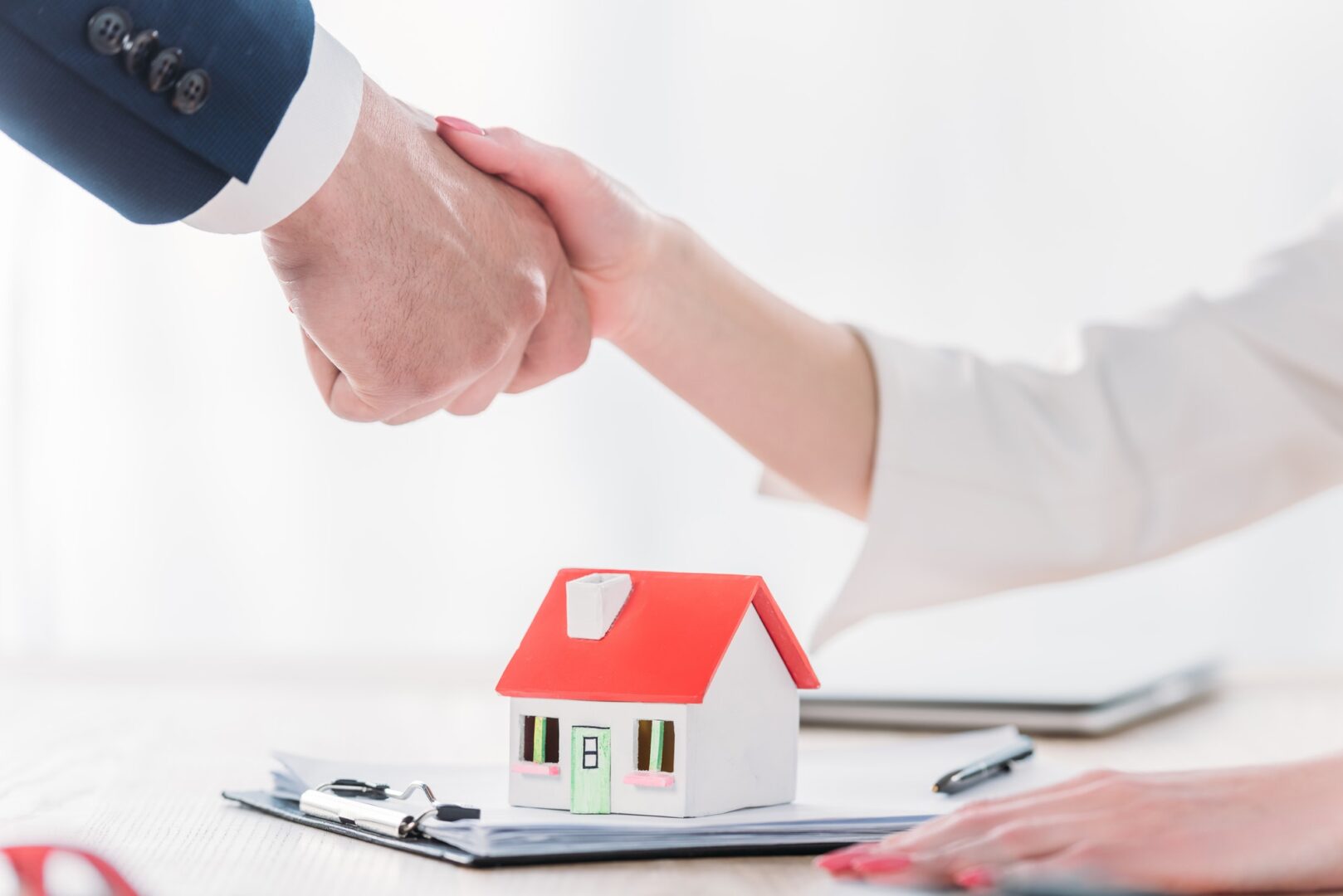 cropped shot of realtor shaking hands with client near house model on tabletop